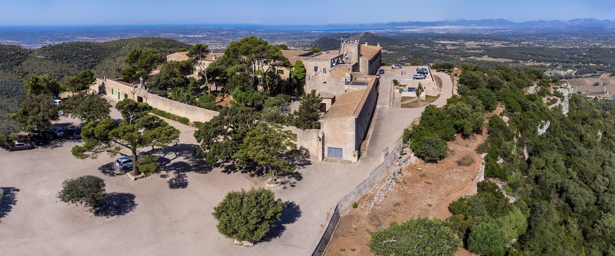 An aerial view of a historic fortress with surrounding greenery and a distant cityscape.