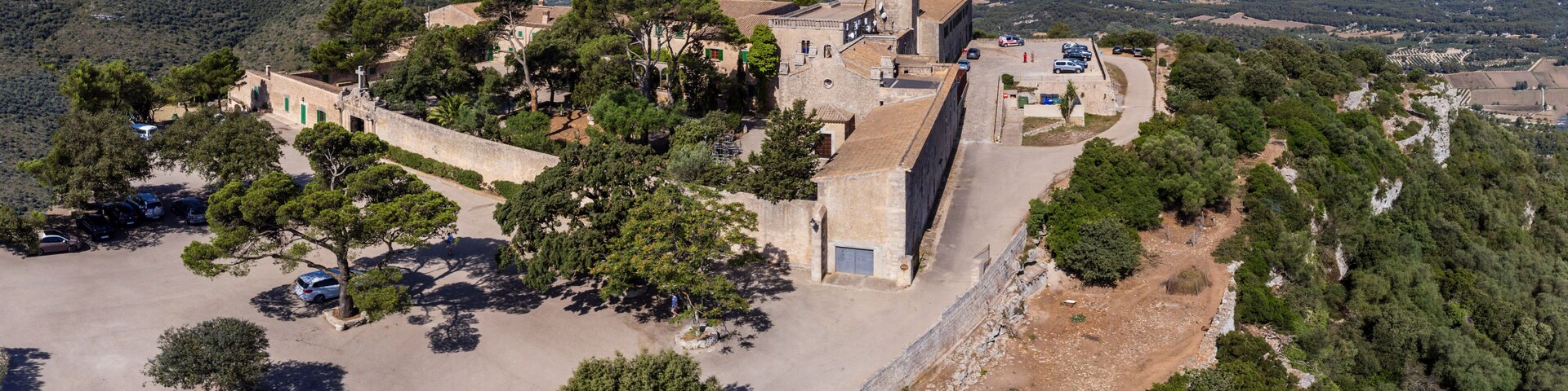 An aerial view of a historic fortress with surrounding greenery and a distant cityscape.