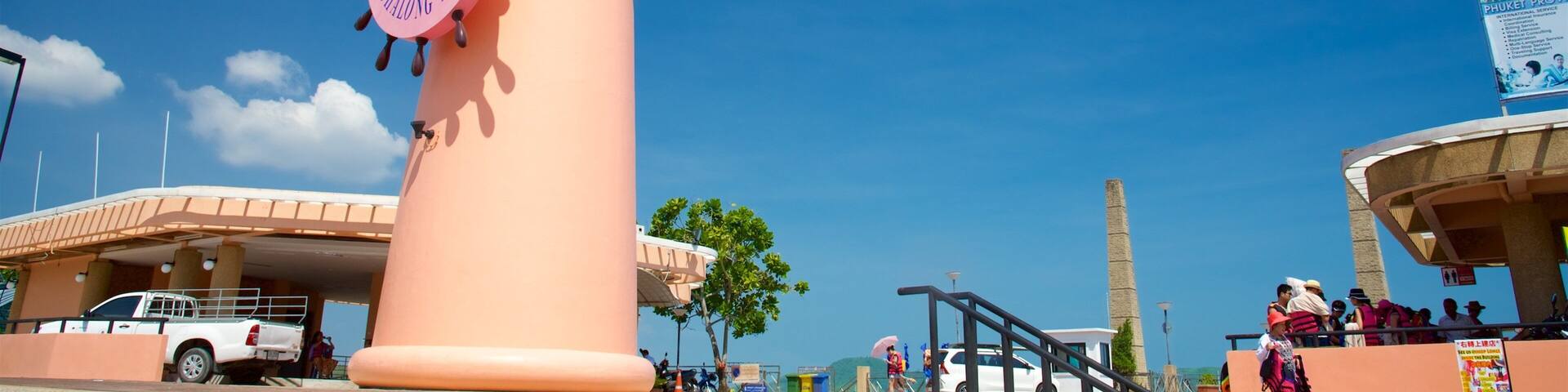 A pink lighthouse with a circular sign, a white truck, and people in the background.