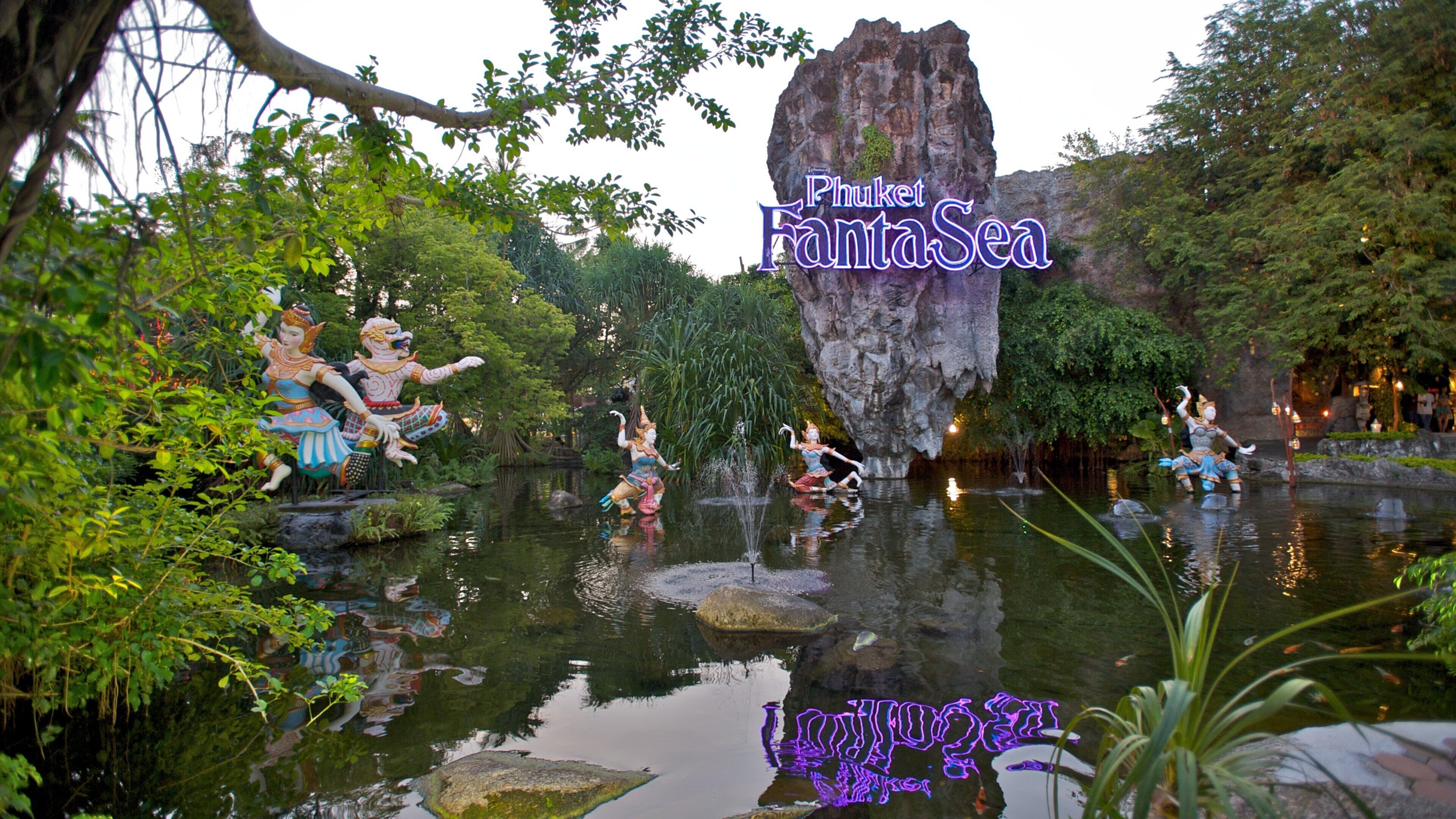 A water feature with statues, a large rock formation, and lush greenery.