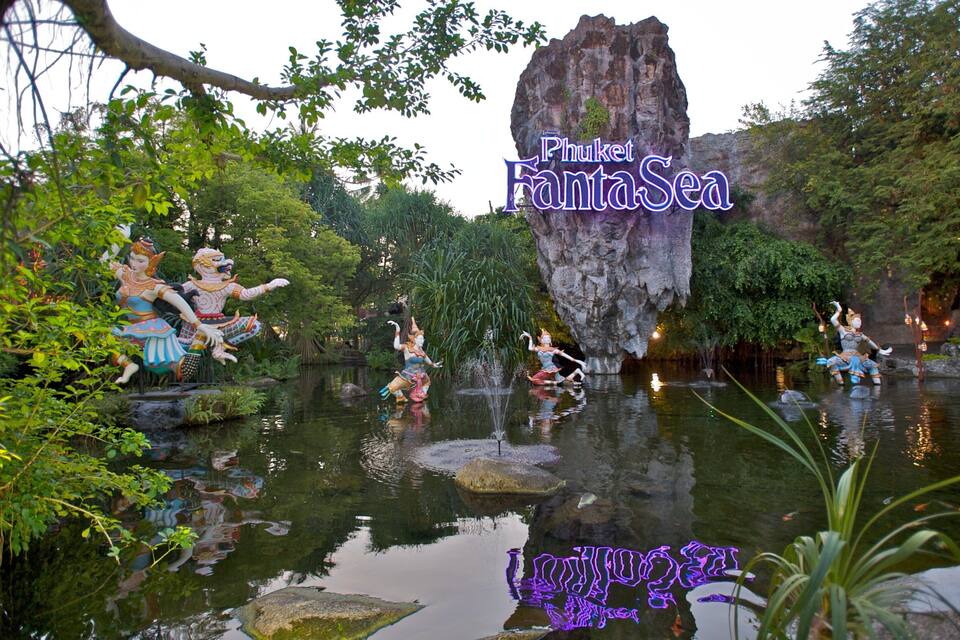 A water feature with statues, a large rock formation, and lush greenery.