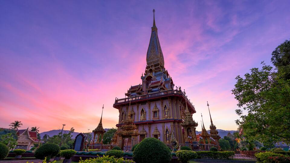 A temple with a pointed spire, surrounded by lush greenery and palm trees.