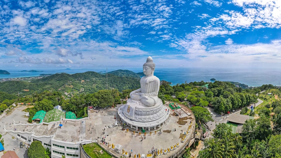 A large white statue surrounded by lush greenery and a coastal landscape.