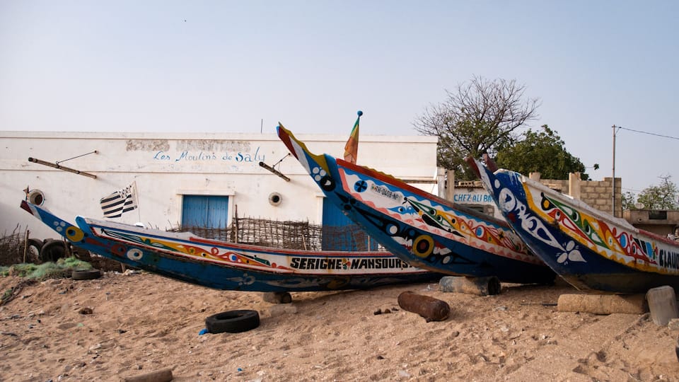 Colorful boats with graffiti, a white building with a blue door, and a barren landscape.