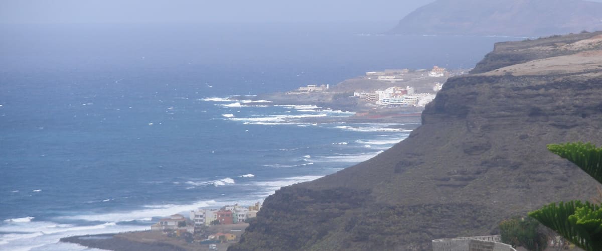 A coastal landscape with a rugged cliff, ocean waves, and a small settlement.