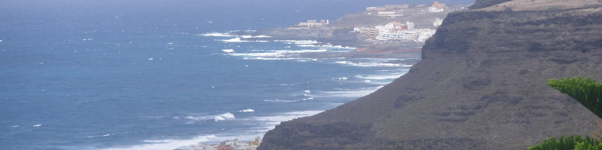 A coastal landscape with a rugged cliff, ocean waves, and a small settlement.
