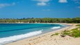 A beach with clear turquoise water, sandy shore, and green vegetation.