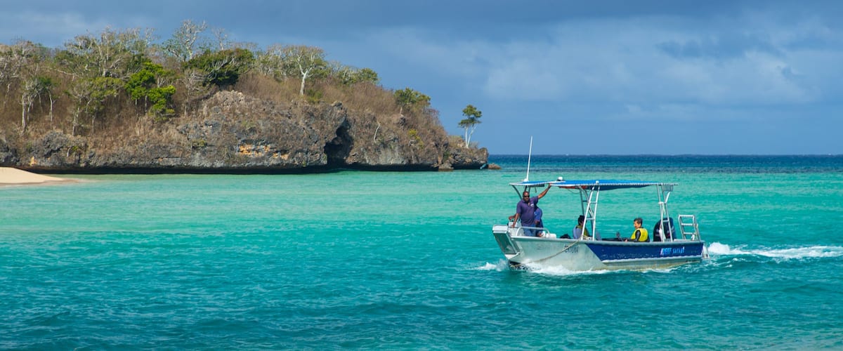 Un bateau sur des eaux turquoise, près d’une île rocheuse à la végétation clairsemée.