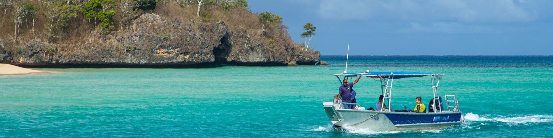 A boat on turquoise waters near a rocky island with sparse vegetation.