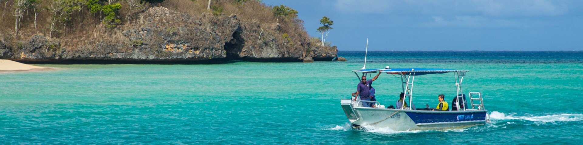 Un bote sobre aguas turquesas cerca de una isla rocosa con vegetación escasa.