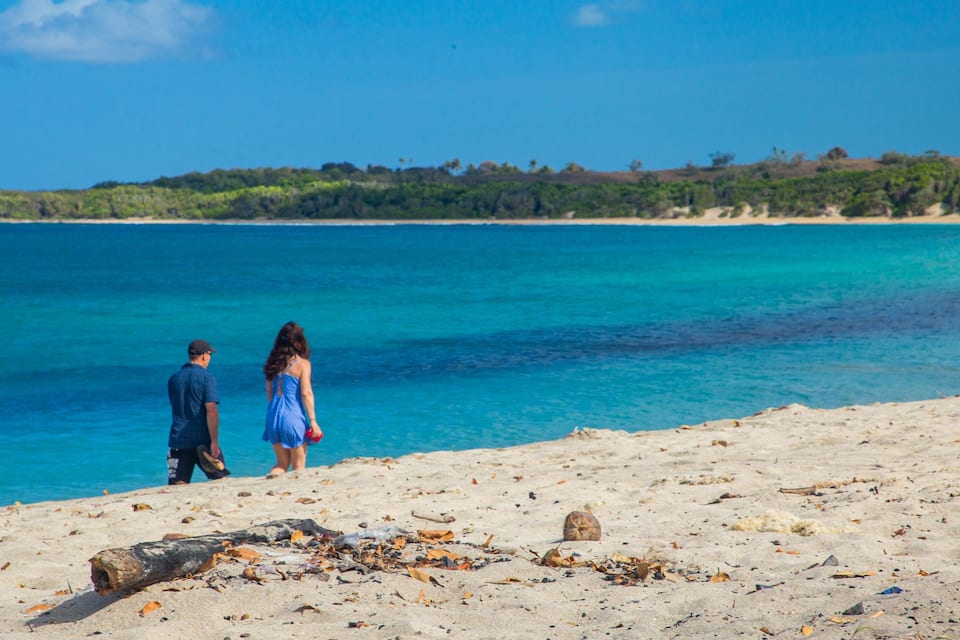 Una playa con agua turquesa cristalina, una orilla arenosa y una costa boscosa en la distancia.