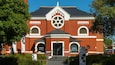 A red brick building with a large circular stained glass window, a white entrance, and a small bell tower.