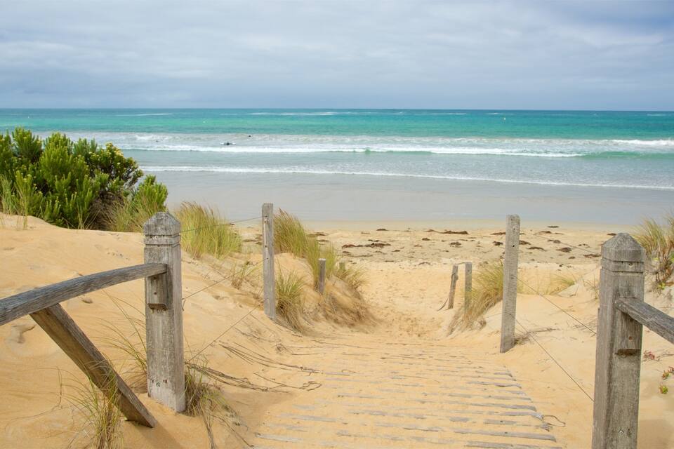 A wooden staircase leading to a sandy beach with ocean waves in the background.
