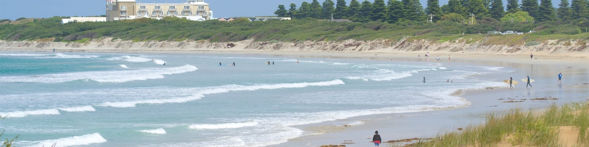 A beach with waves, a building, and trees.