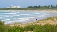 A beach with waves, a building, and trees.