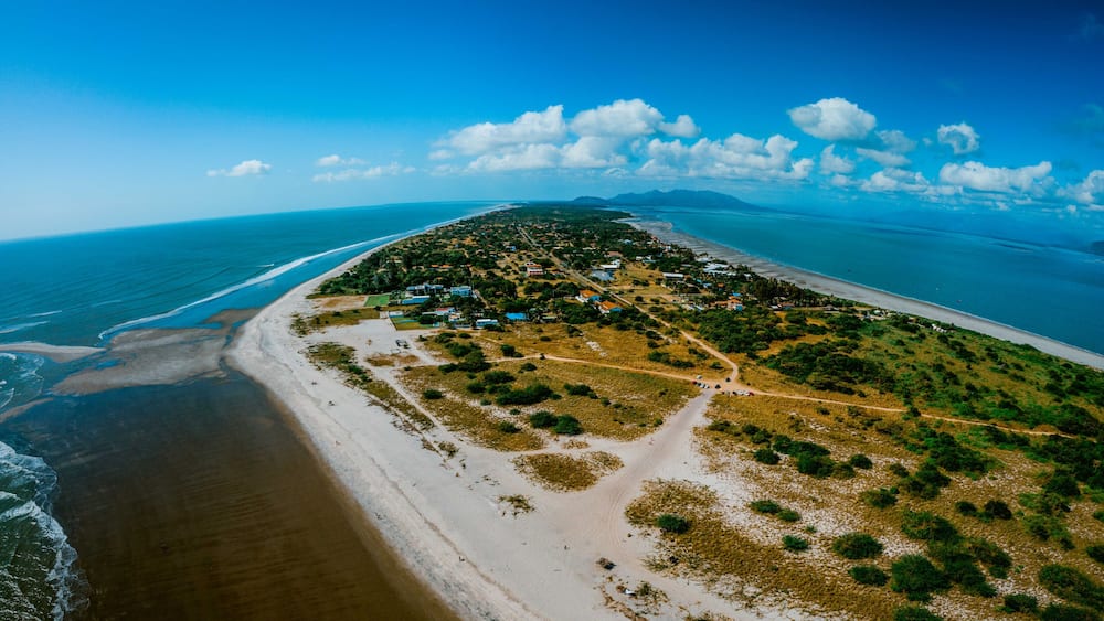 A coastal landscape with a beach, a small settlement, and a clear blue sky.