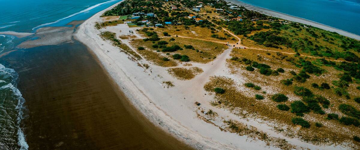 A coastal landscape with a beach, a small settlement, and a clear blue sky.