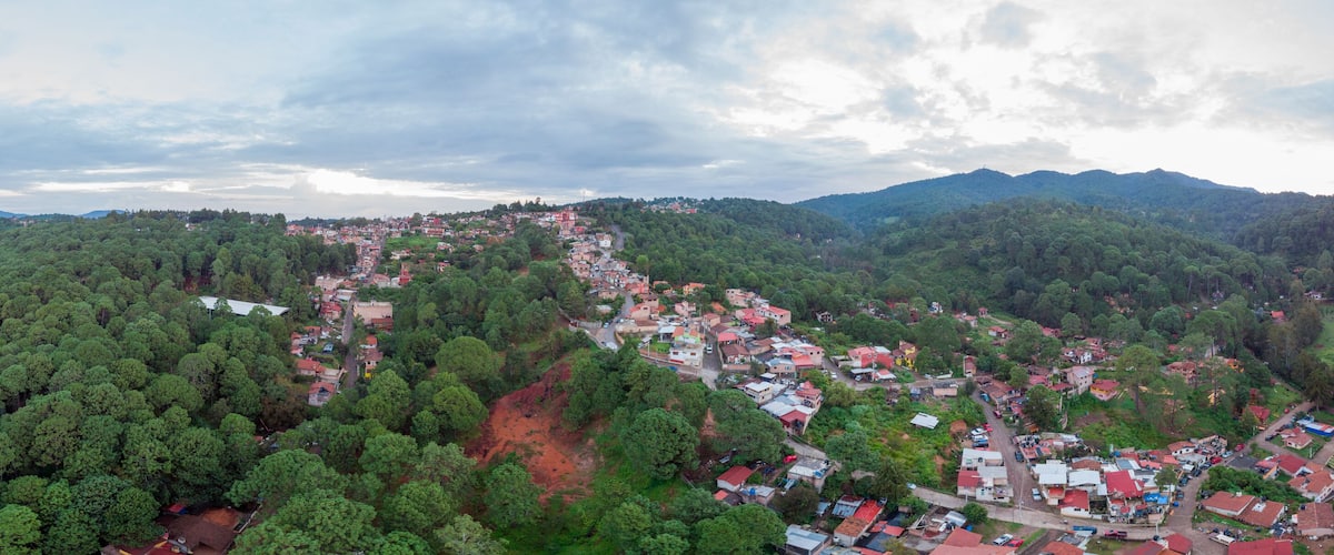 A mountainous landscape with a village nestled among dense forests and red soil patches.