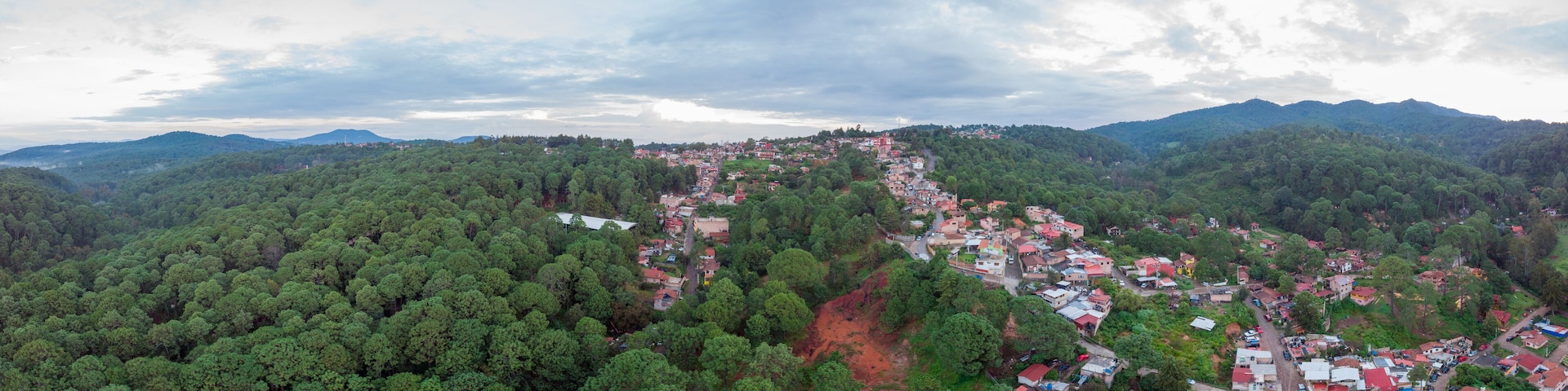 A mountainous landscape with a village nestled among dense forests and red soil patches.