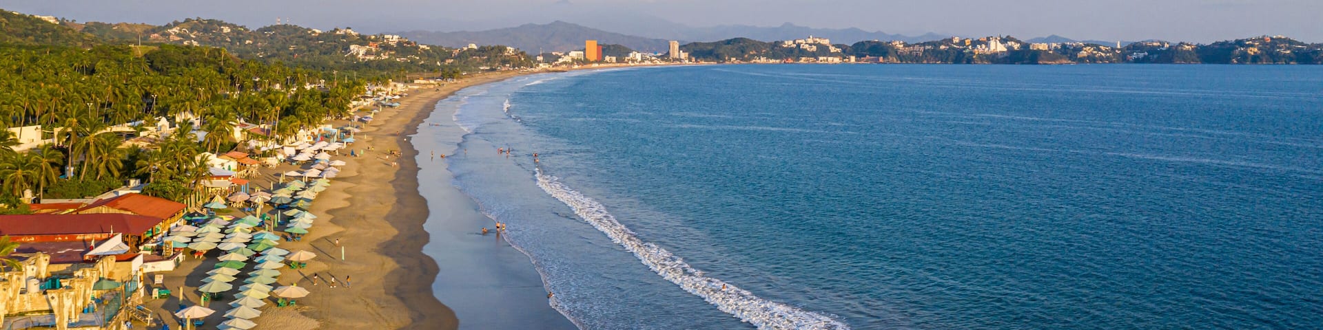 A coastal beach with umbrellas, palm trees, and a clear sky.
