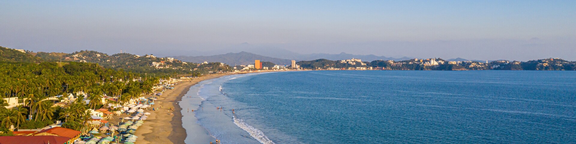 Una playa costera con sombrillas, palmeras y un cielo despejado.