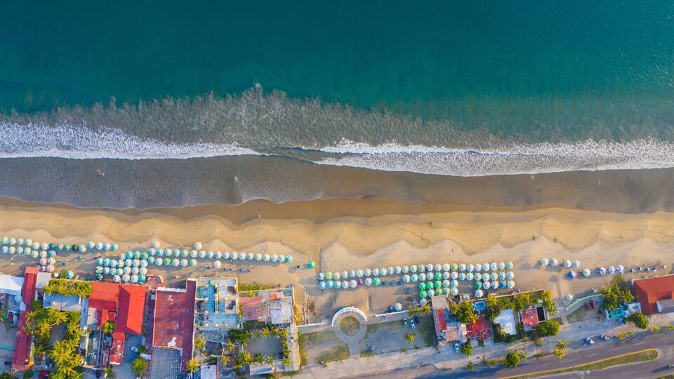 An aerial view of a beach with umbrellas, buildings, and a road.