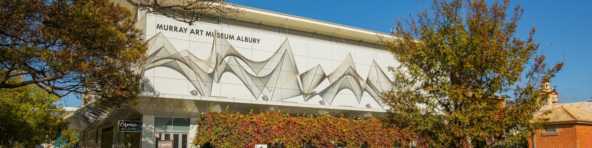 The Murray Art Museum Albury building with a unique architectural design, surrounded by trees and a grassy area.