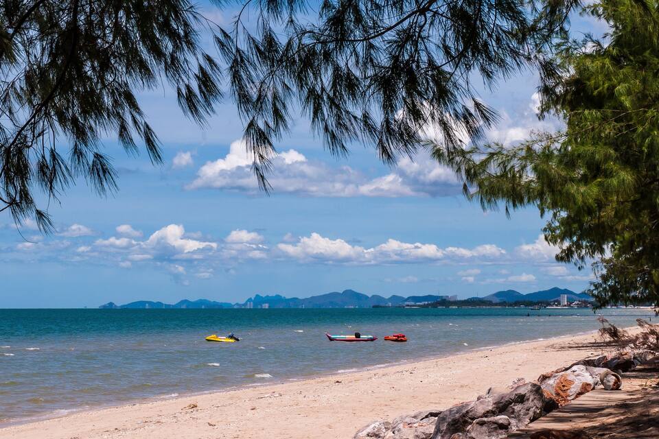 Una playa con barcos, cielo despejado y montañas a lo lejos.