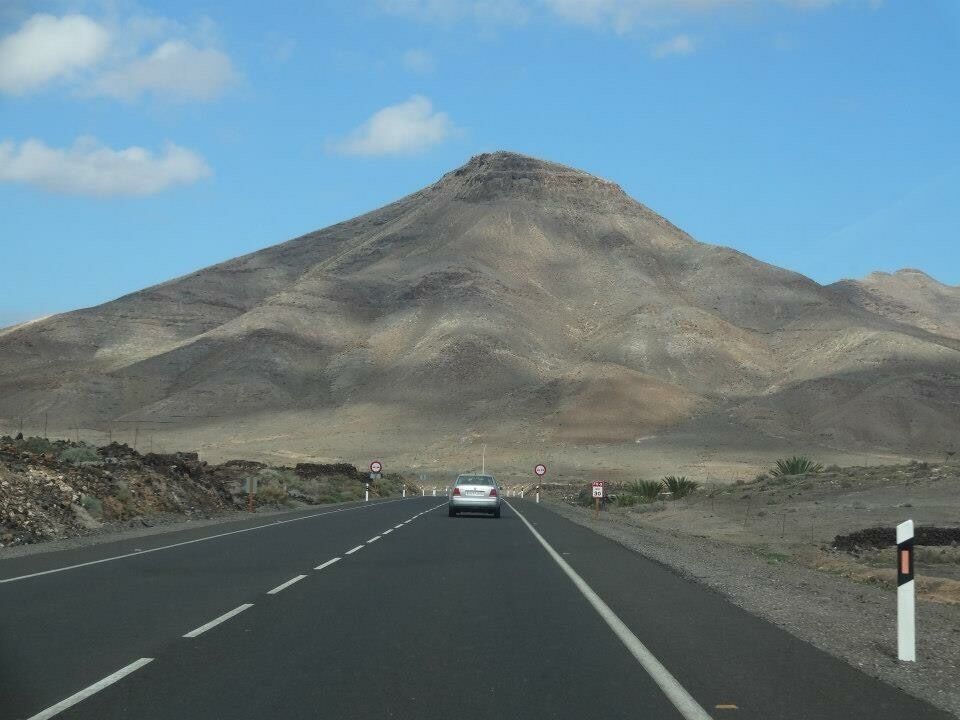 A road with a car driving towards a mountain.
