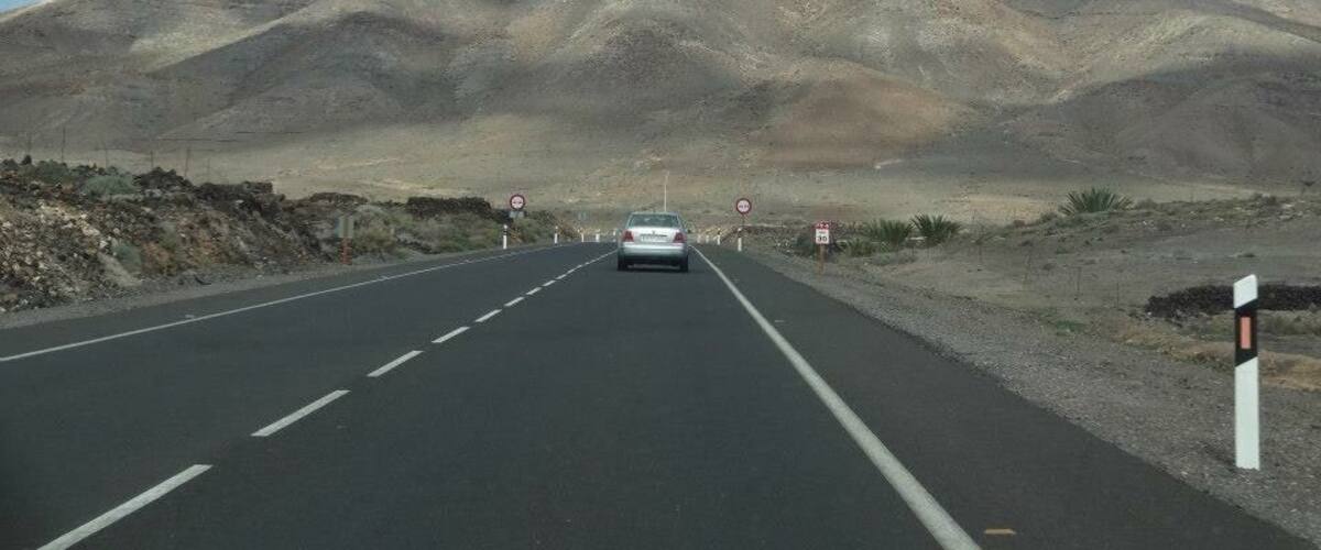 A road with a car driving towards a mountain.