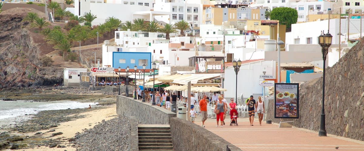 A coastal town with white buildings, a beach, and a rocky cliff.