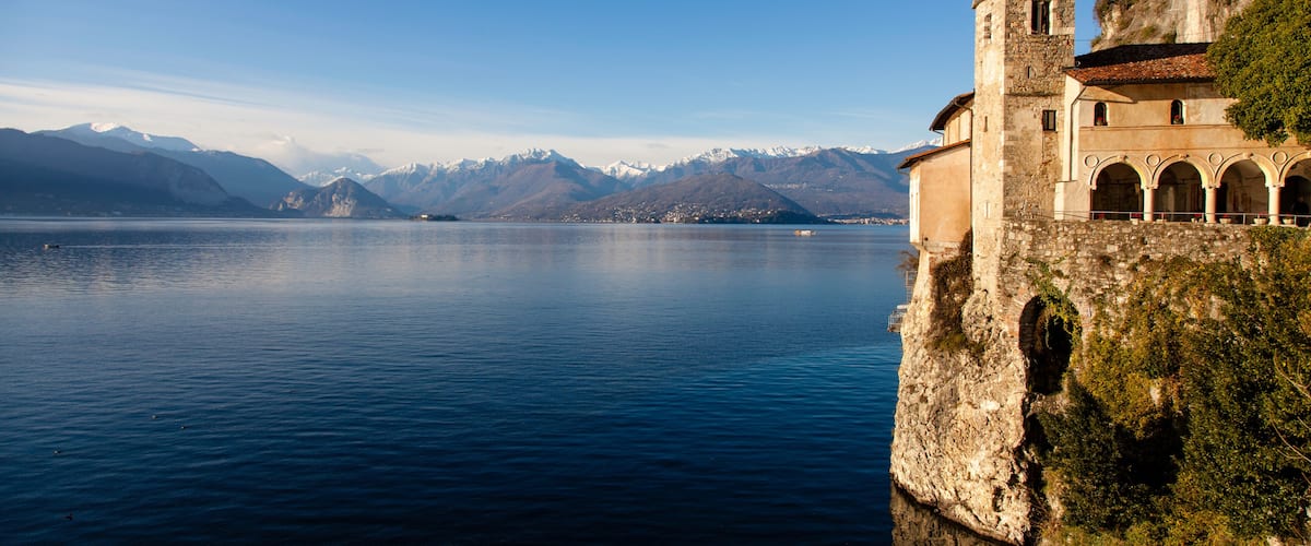 A historic building with a bell tower overlooking a calm lake with mountains in the background.