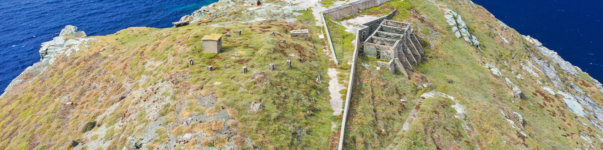 A coastal landscape with a lighthouse, a stone structure, and a grassy cliff.