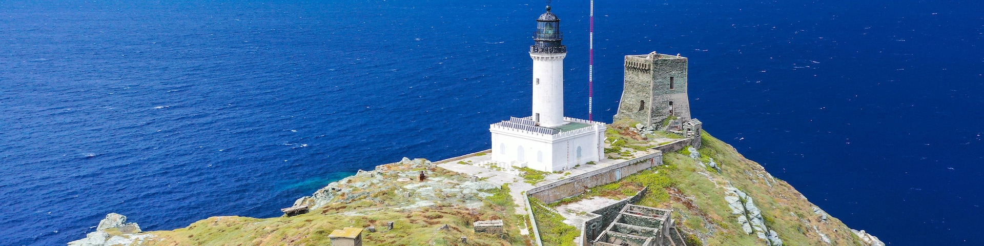 Un paisaje costero con un faro, una estructura de piedra y un acantilado cubierto de hierba.