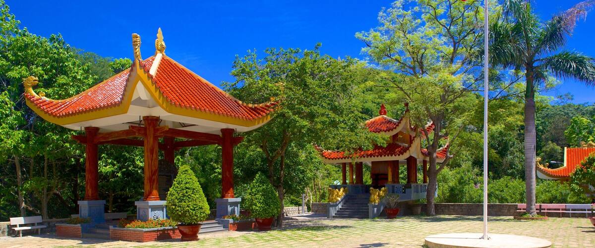 A traditional pavilion with a red roof and golden dragon decorations, surrounded by lush greenery and a clear blue sky.