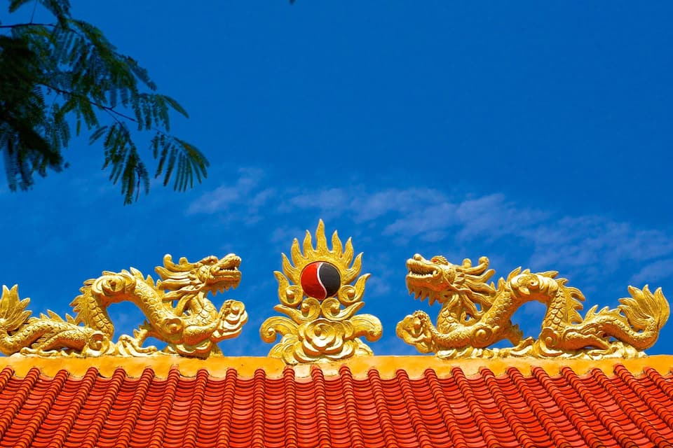 Un toit traditionnel orné de sculptures de dragons dorés et d’un emblème rouge et noir.