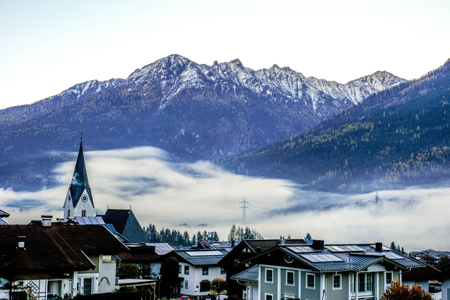 Ein Dorf mit traditionellen Häusern, einer Kirche mit Kirchturm und schneebedeckten Bergen im Hintergrund.