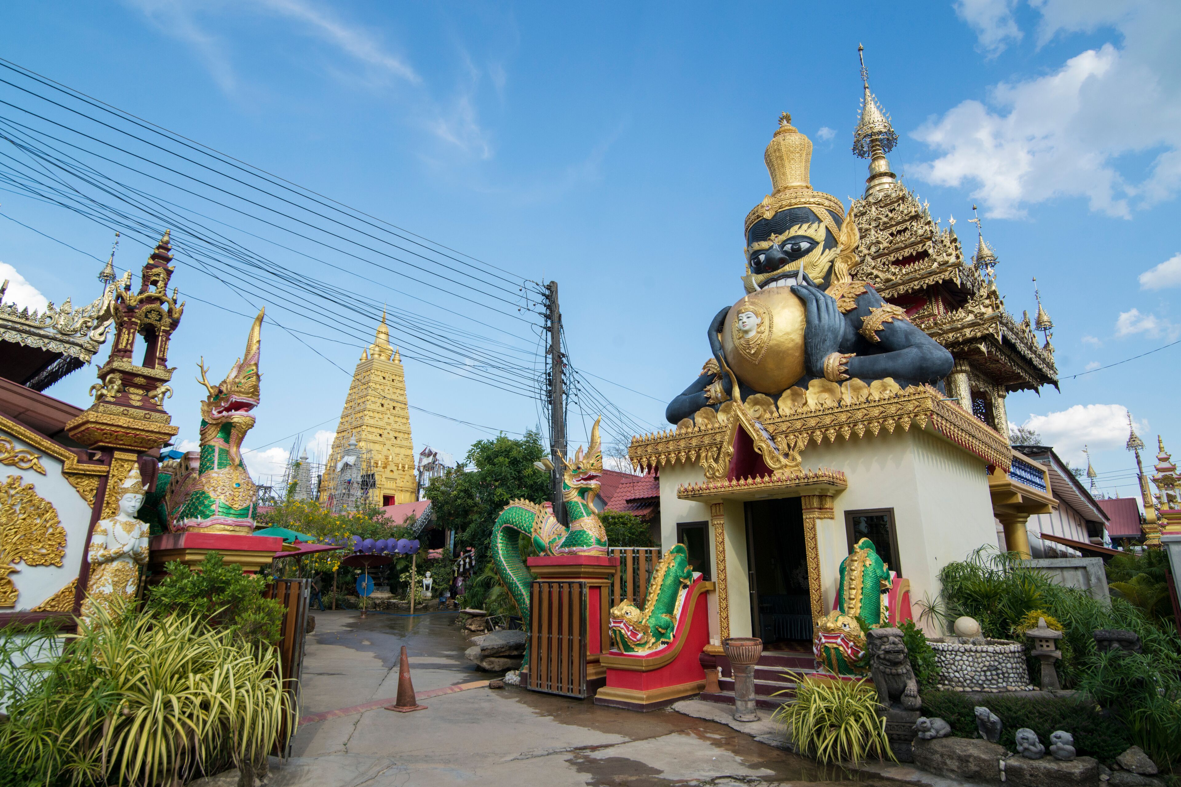 A temple with golden spires, a large dragon statue, and traditional Thai architecture.