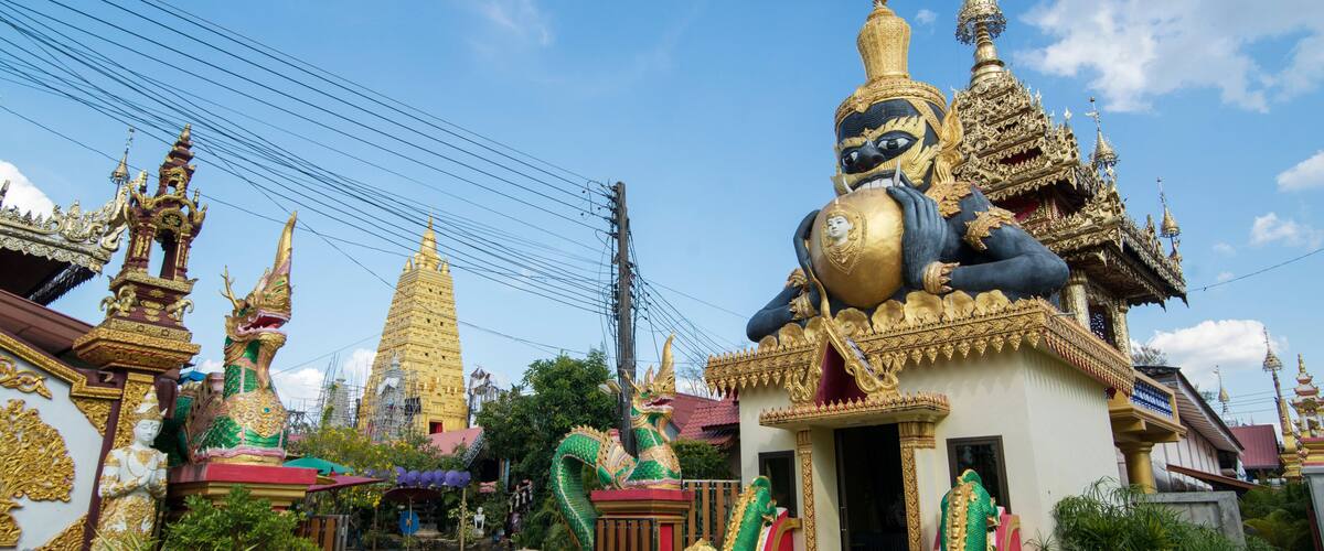 A temple with golden spires, a large dragon statue, and traditional Thai architecture.