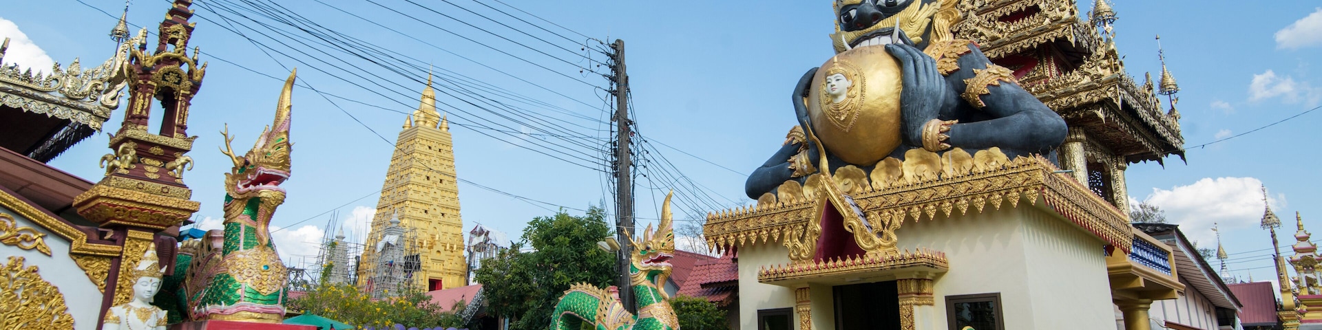 A temple with golden spires, a large dragon statue, and traditional Thai architecture.