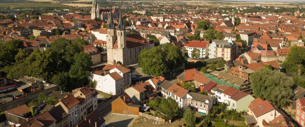 A town with a prominent church tower, surrounded by red-roofed buildings and green trees.