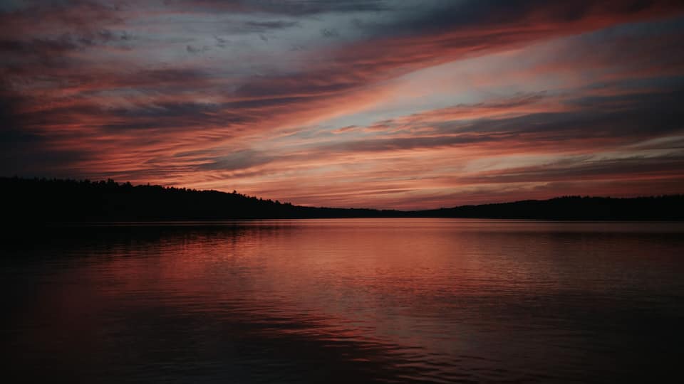 A sunset over a calm lake with a silhouette of a forested shoreline.