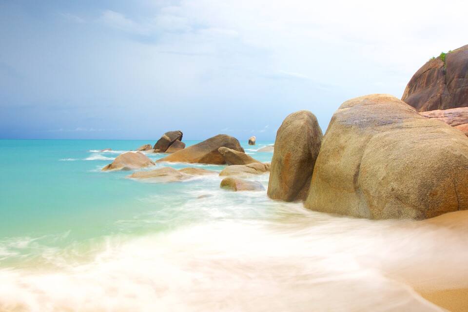 A beach with large rocks and turquoise water.