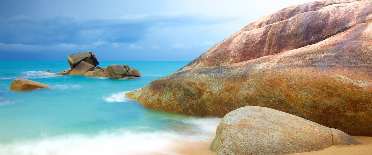 A beach with large rocks and clear turquoise water.
