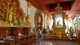 A temple interior with golden statues, a central altar, and intricate wall carvings.