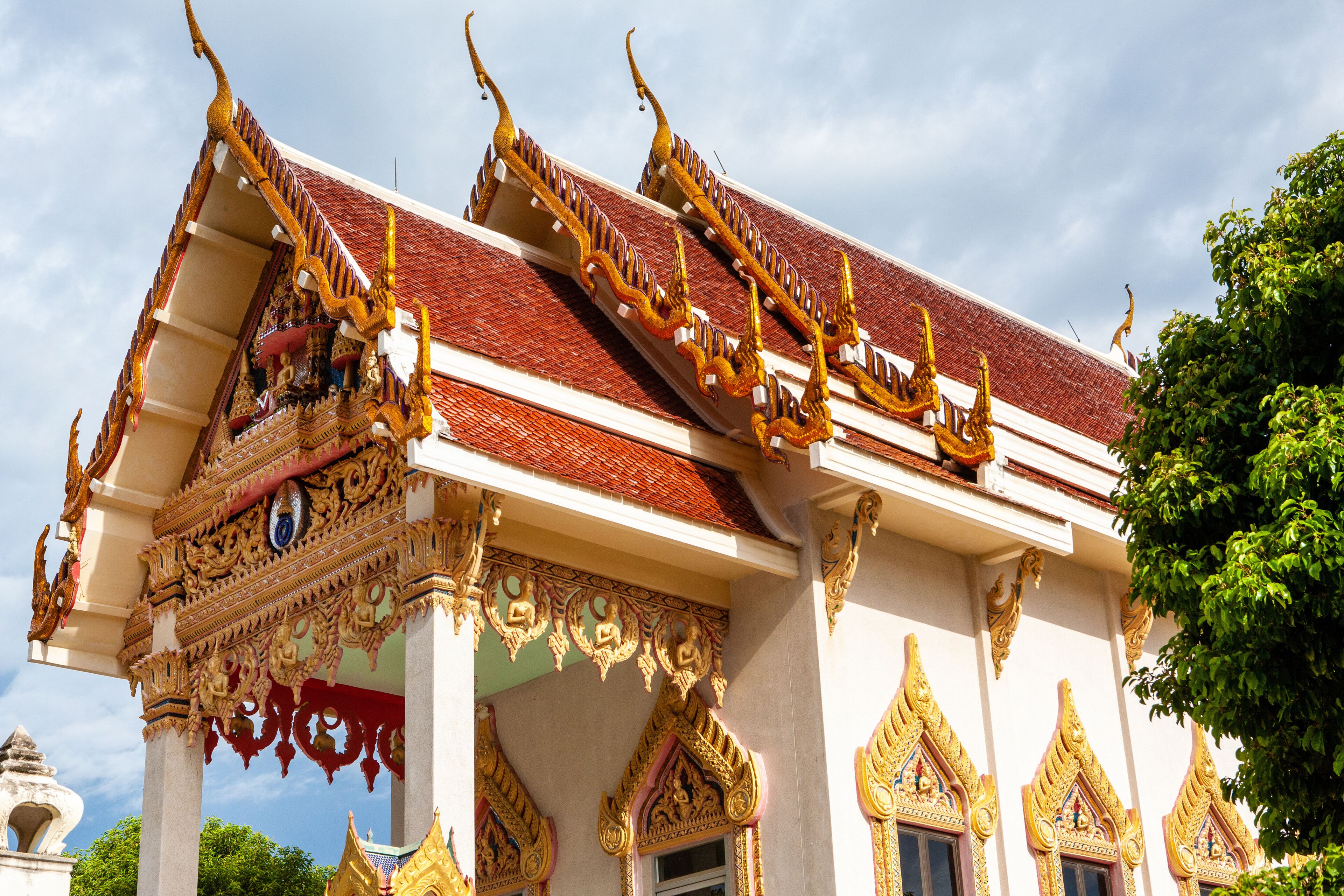 A traditional Thai temple with ornate golden decorations and a red roof.