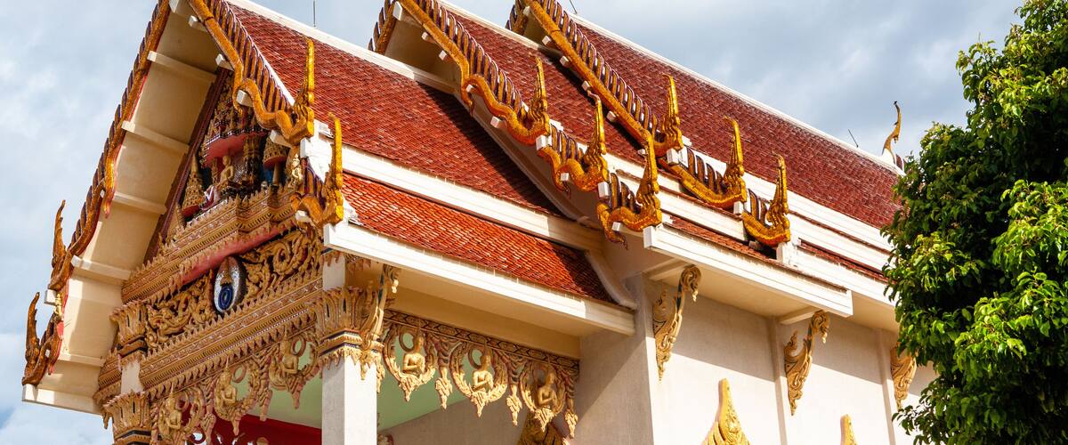 A traditional Thai temple with ornate golden decorations and a red roof.