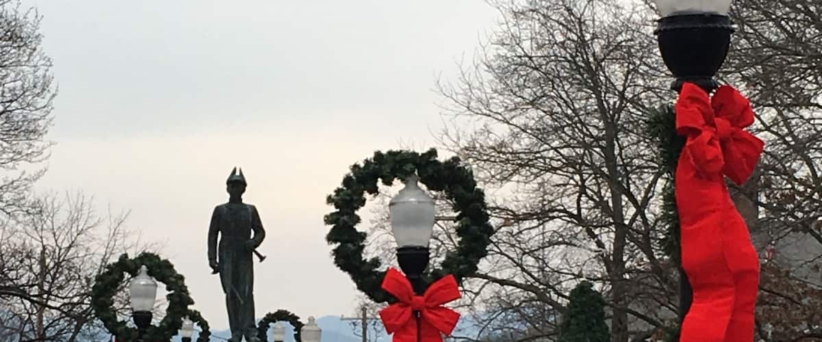A statue in a park with red ribbons and wreaths.