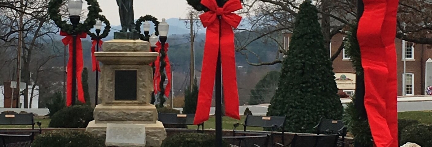 A statue in a park with red ribbons and wreaths.