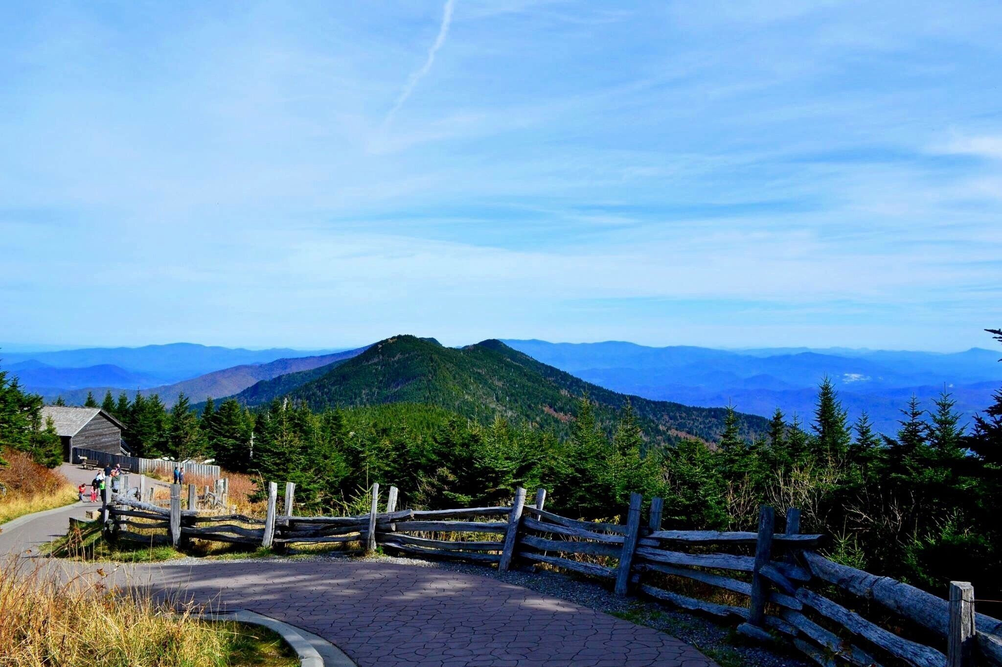 A mountain landscape with a wooden fence, a paved path, and a small building.